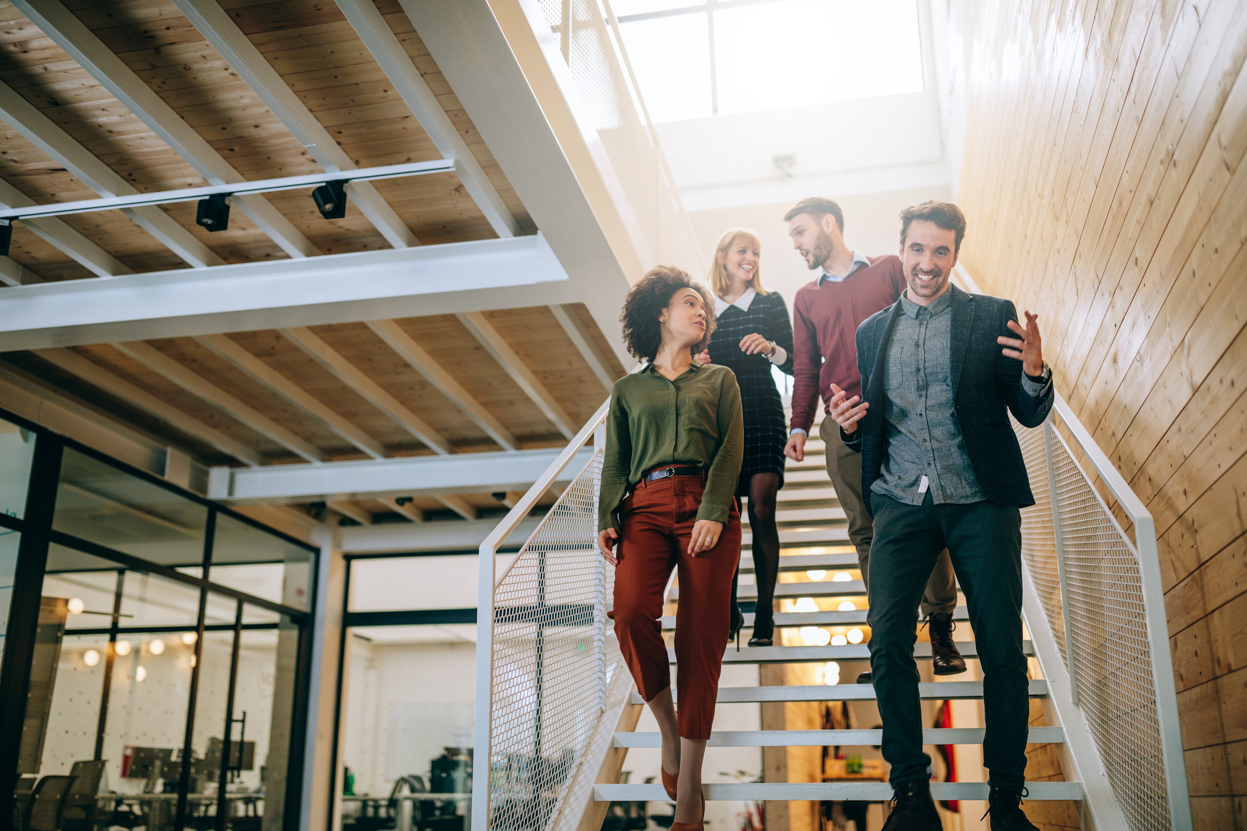 Four people in business-casual attire walking down a staircase in a modern office environment