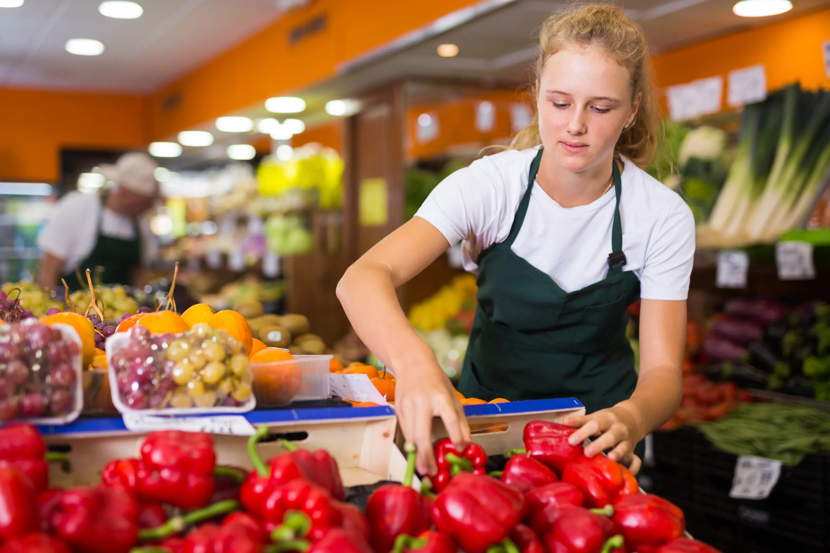 Grocery store employee stocking a shelf with red peppers
